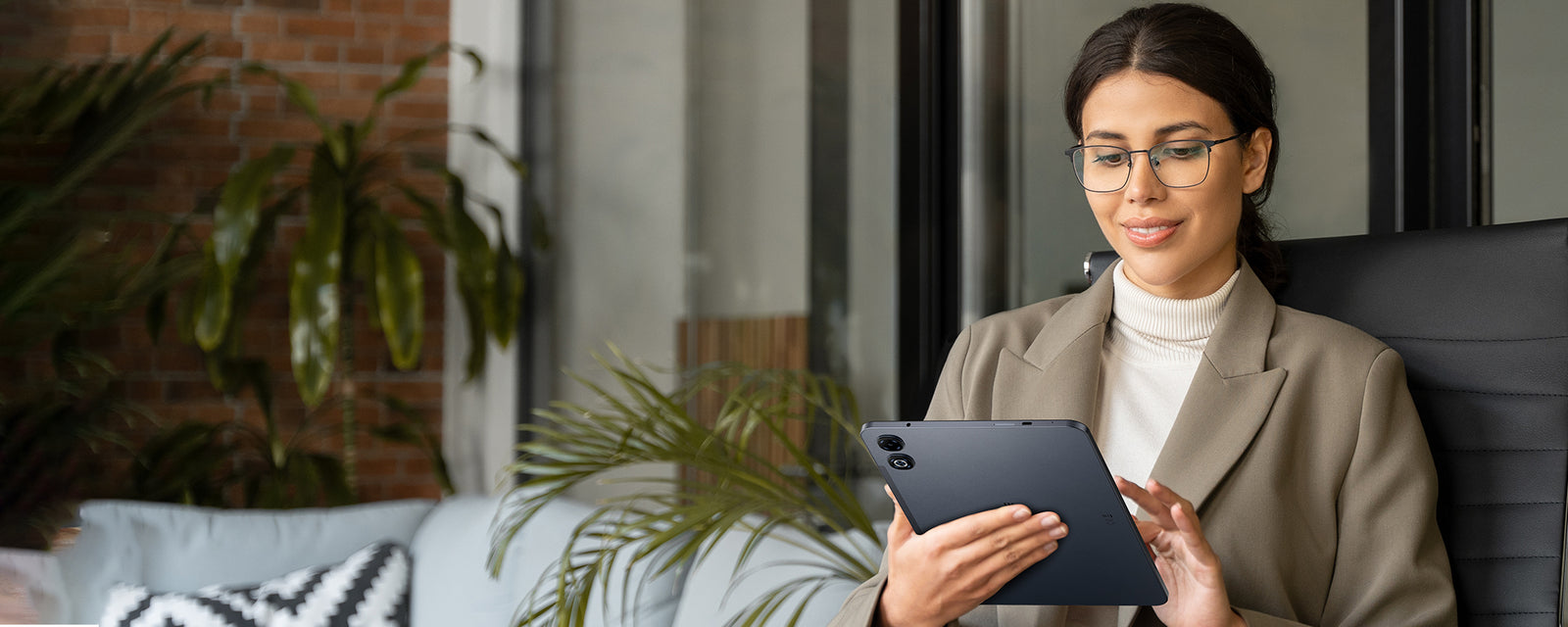 Woman using a tablet in an office setting with plants and furniture.